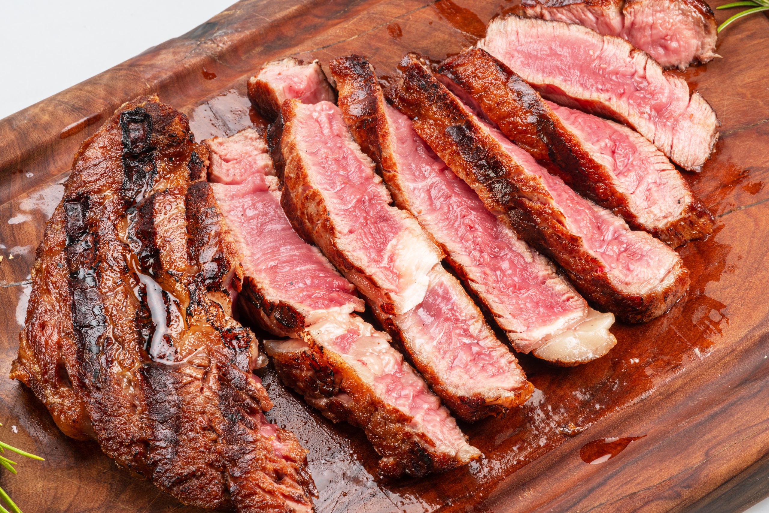 Sliced grilled beef ribeye steak medium rare on wooden cutting board with rosemary.